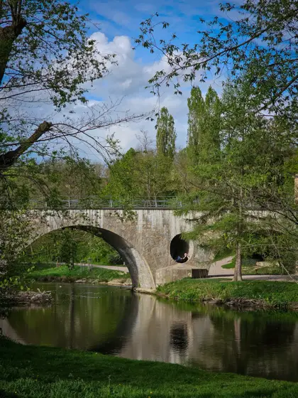 Puente y follaje reflejados en el agua quieta.