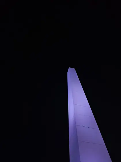 Un monumento vertical iluminado en violeta durante la noche.
