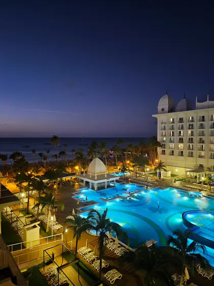 Hotel, piscina y palmeras: reflejos de luz al anochecer.