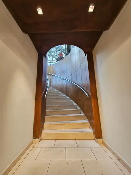 Escalera curva de madera al fondo de un pasaje abovedado.